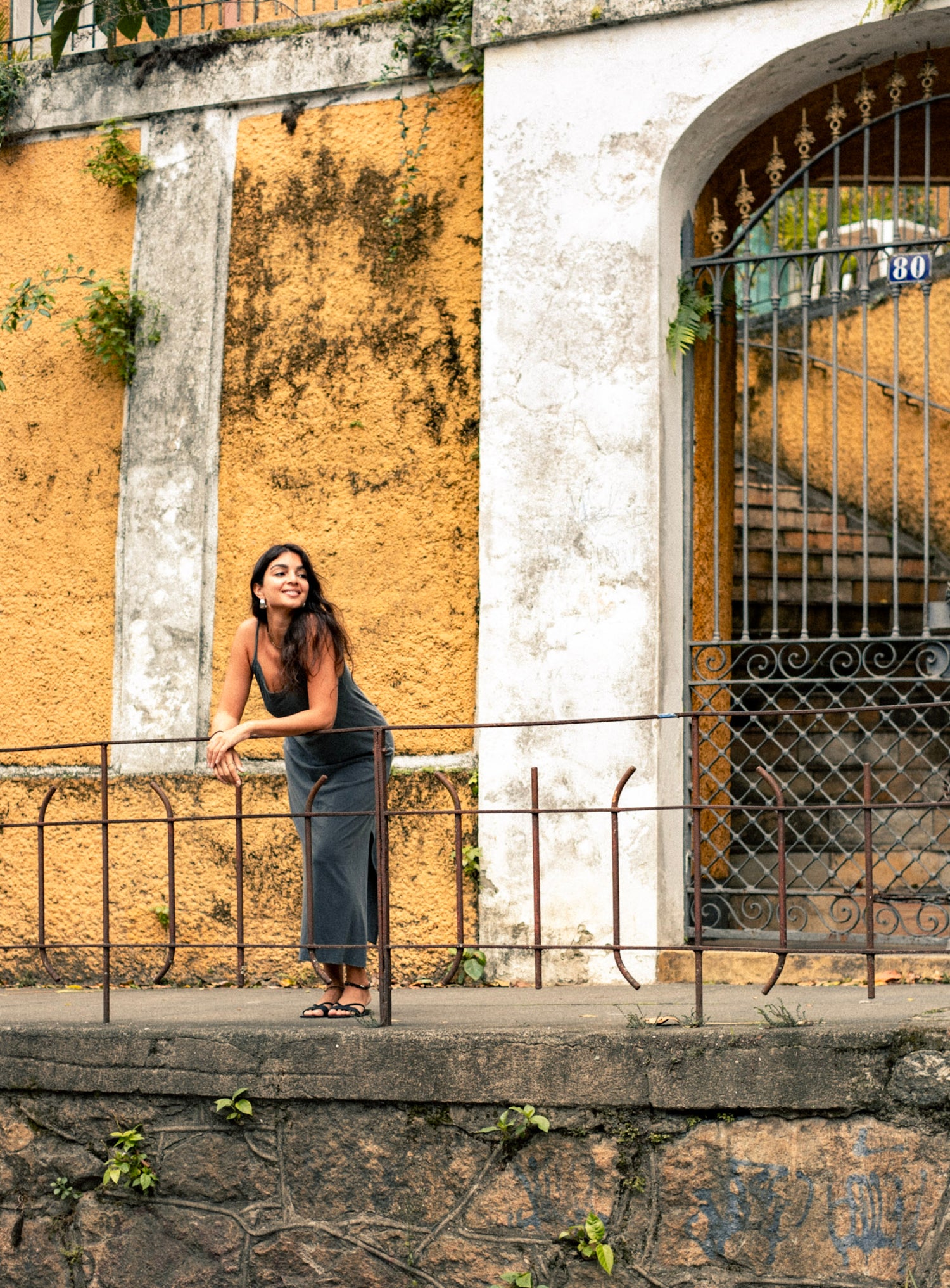 Woman leaning against a railing with a yellow wall and decorative gate in the background