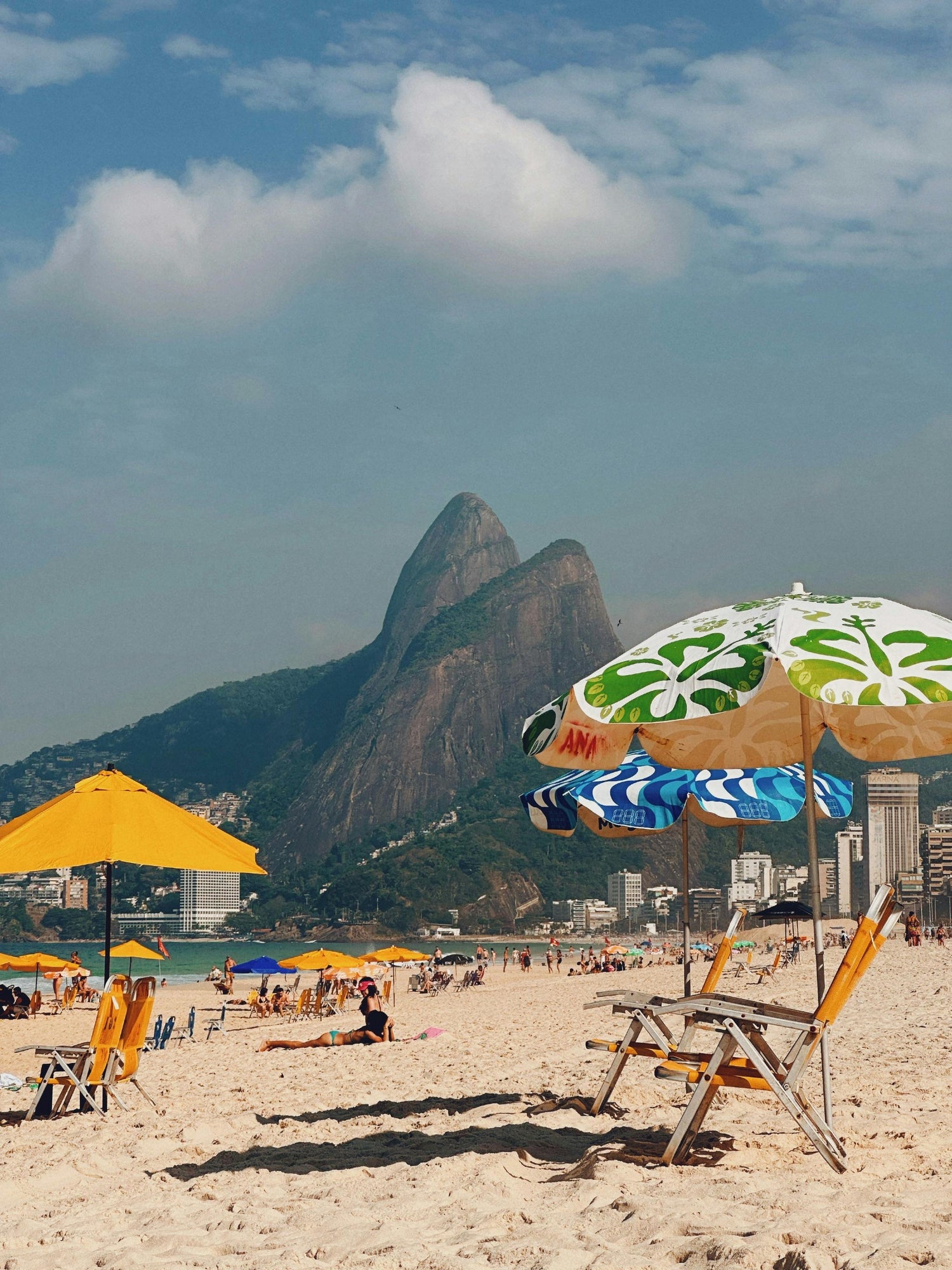 Beach scene with colorful umbrellas, lounge chairs, and mountainous landscape.